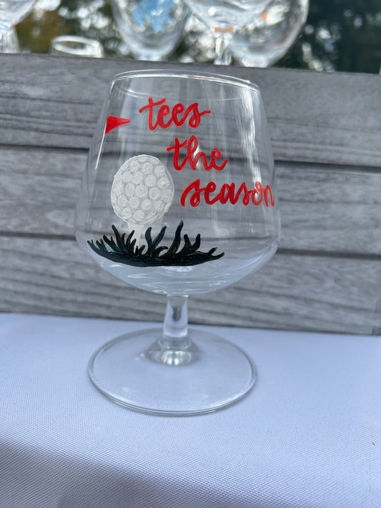 Hand-painted manhattan cocktail glass with holiday design, painted golf ball and red flag with "tees the season" written in calligraphy. 