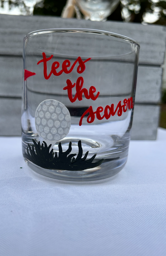 Golf holiday themed manhattan golf glass with golf ball and red flag painting and "tees the season" written in calligraphy